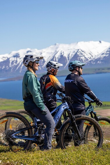 Three cyclists on a mountain bike trail with a lake and snow-capped mountains in the background. 3