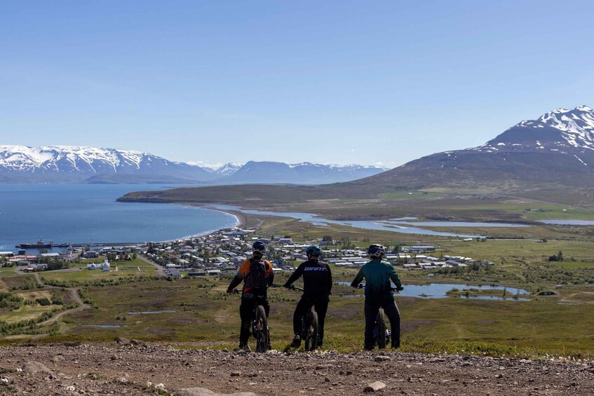 Three mountain bikers on a trail with a coastal town and mountains in the background. 5