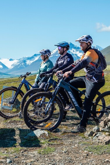 Three mountain bikers on a trail with snow-capped mountains in the background. 5