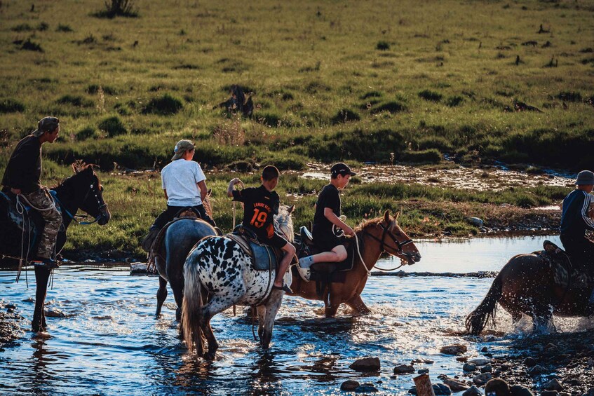 People riding horses through a shallow stream in a grassy field. 3