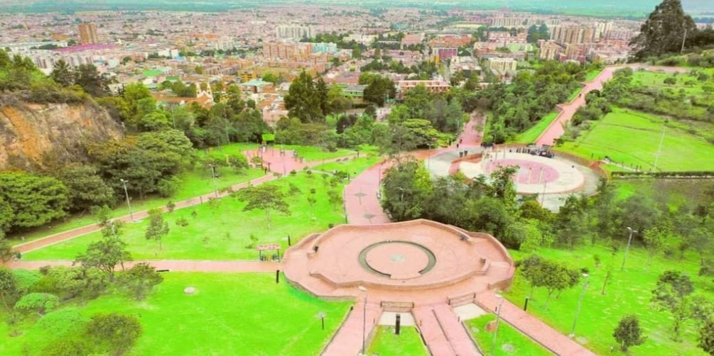 A park with a central circular monument, green pathways, and surrounding buildings. 1