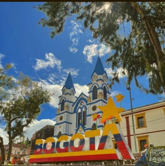 A colorful street scene with a large sign reading 'BOGOTA' and a church with blue and white architecture. 5