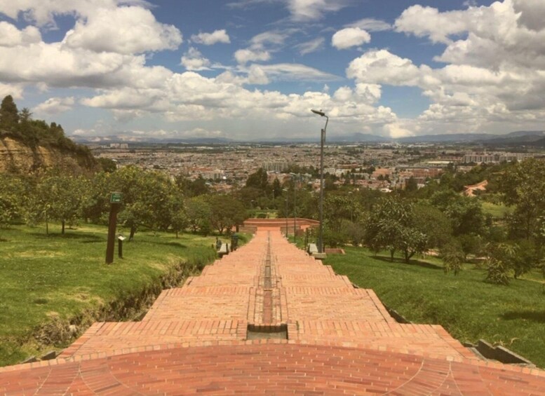 A paved pathway leading towards a cityscape under a partly cloudy sky. 2
