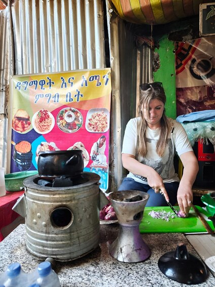 A person cooking with a large pot and cutting board, a food poster, and a small stove. 1
