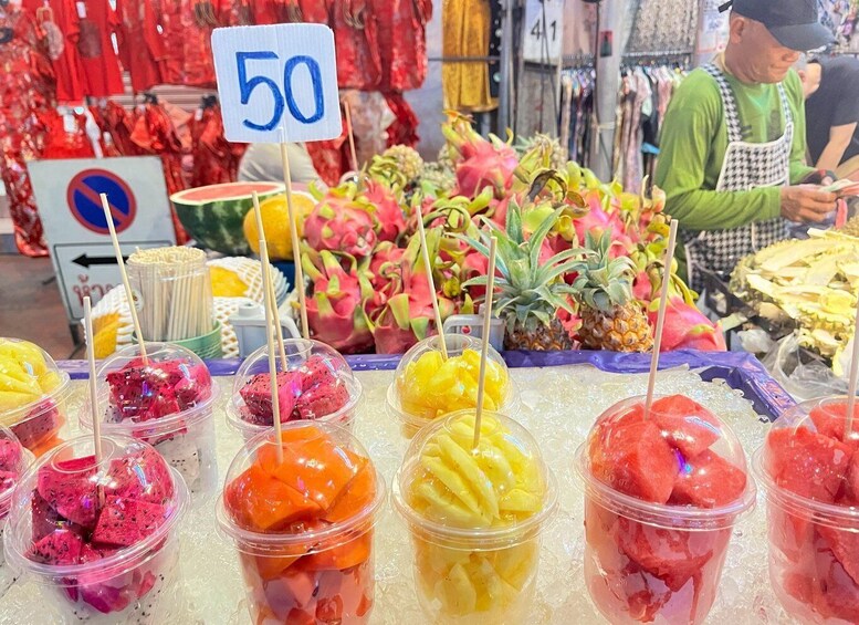 A market stall with colorful fruit-based drinks in plastic cups, a price sign of 50, and a no parking sign in the background. 5