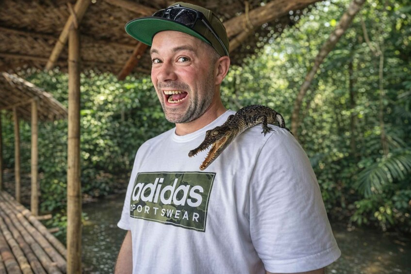 Eine Person, die ein weißes T-Shirt mit dem Aufdruck 'adidas sportwear' trägt, steht draußen, mit einem grünen Hut und einem Kriechtier auf der Schulter. 3
