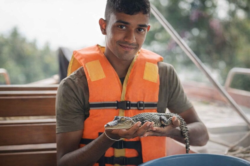 Eine Person trägt eine orangefarbene Warnweste und hält ein Reptil. 1