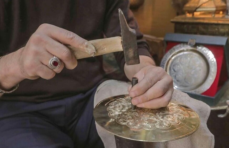 A person using a hammer and chisel on a metal plate with intricate designs. 2
