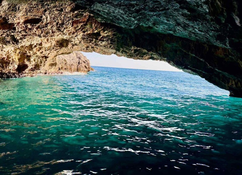 A rocky coastline with a natural arch formation over clear turquoise waters. 4