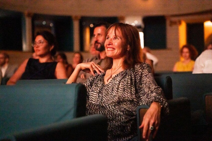 A person seated in a theater with blue seats and a patterned dress. 4