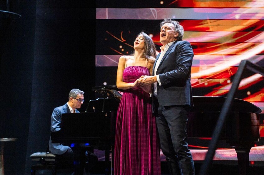 A stage with a piano, a woman in a purple dress, and a man in a suit. 5
