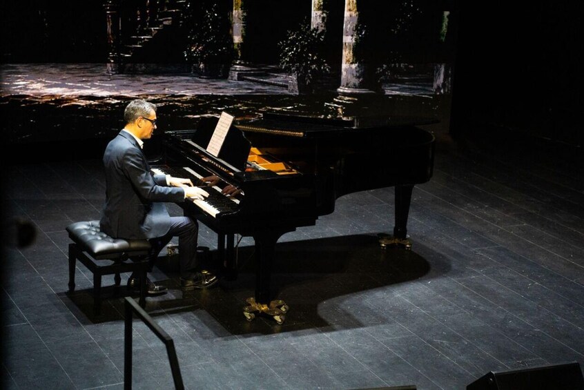 A person playing a grand piano on a stage with a dark background and columns. 2