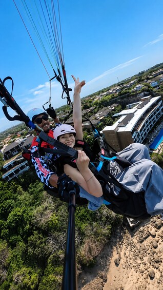 A person in a harness and helmet, suspended by a cable, with a scenic view of a residential area and a bridge in the background. 3