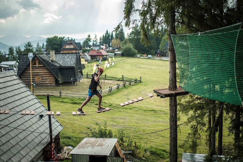 A person on a rope bridge in a rural setting with houses and mountains in the background. 4