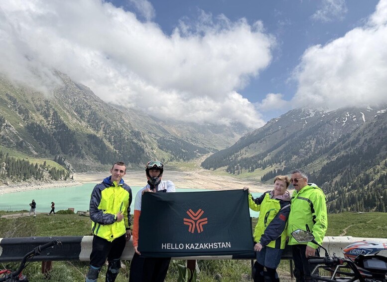 Four people holding a 'HELLO KAZAKHSTAN' banner with a mountainous landscape in the background. 1