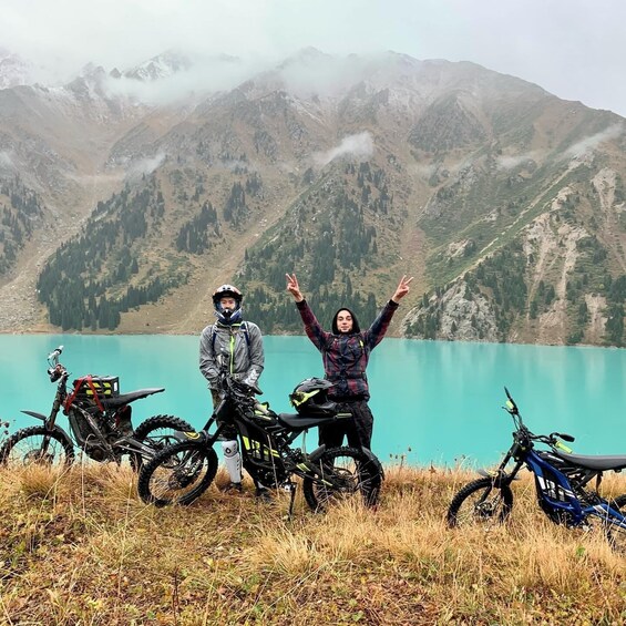 Two people with motorcycles in a mountainous area with a lake. 3