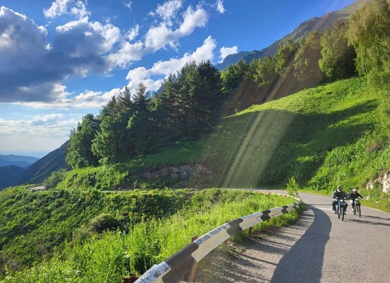 A curving mountain road with cyclists, lush greenery, and a clear sky. 5