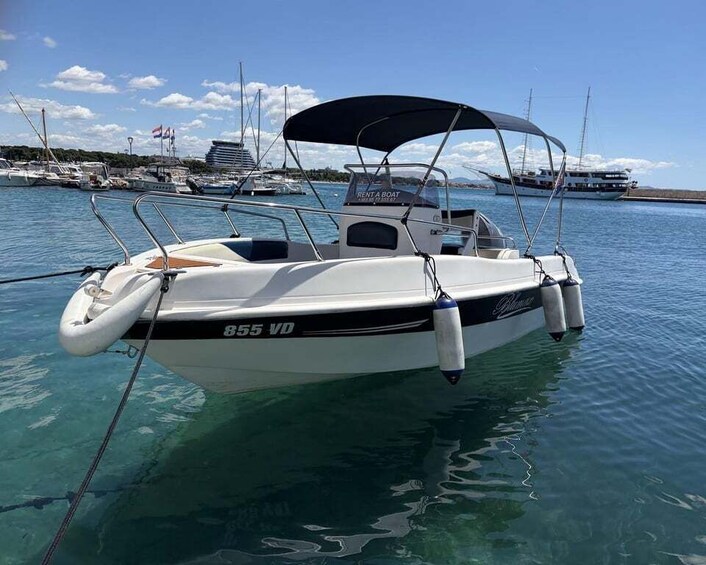 A white boat with '855 VD' on its side, docked in clear water with other boats in the background. 1