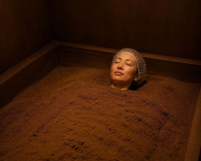 A person lying in a wooden tub filled with sand. 1