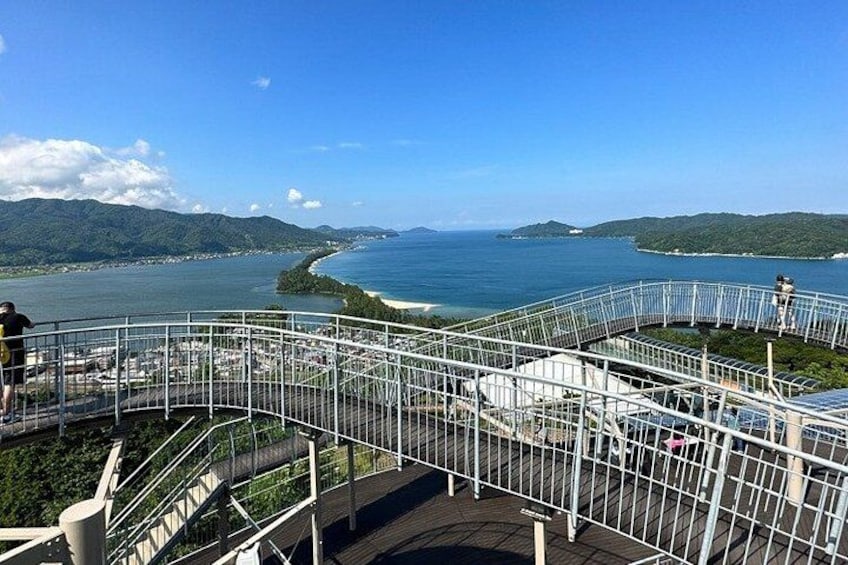A coastal overlook with a metal railing, a view of the sea, and distant hills. 1