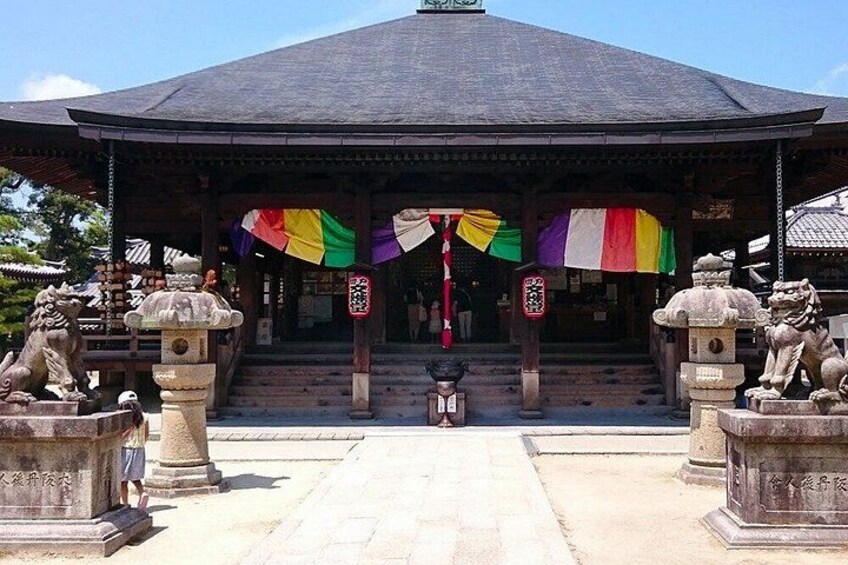 A traditional Japanese building with a tiled roof, stone lion statues, and colorful flags. 5