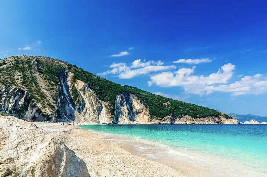 A beach with clear turquoise water, sandy shore, and rocky cliffs. 4