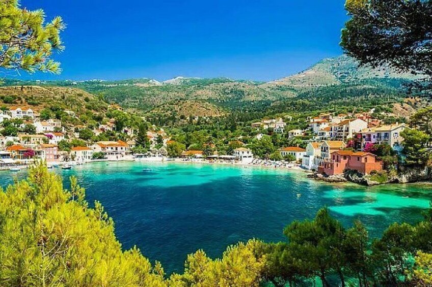 A coastal town with buildings, a clear blue sea, and green hills in the background. 3