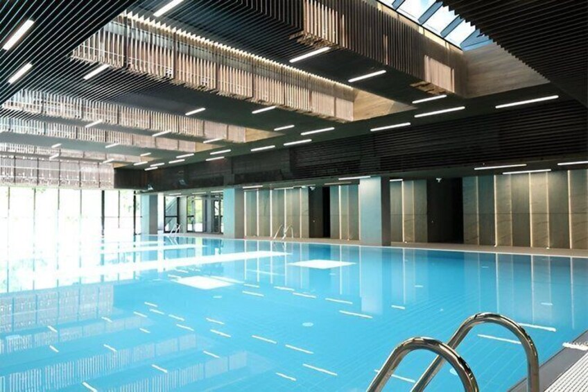 An indoor swimming pool with clear blue water, metal ladders, and a modern ceiling design. 1