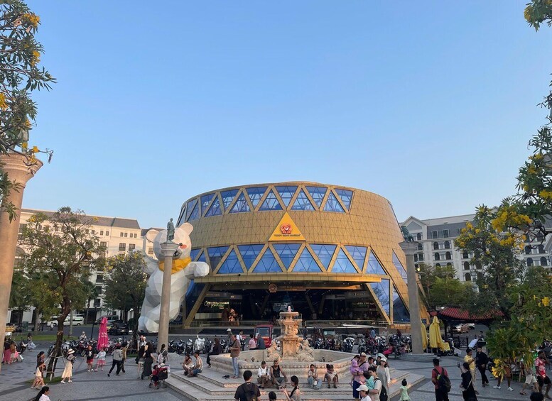 A modern building with a unique geometric facade, surrounded by a plaza with people and a large sculpture. 5