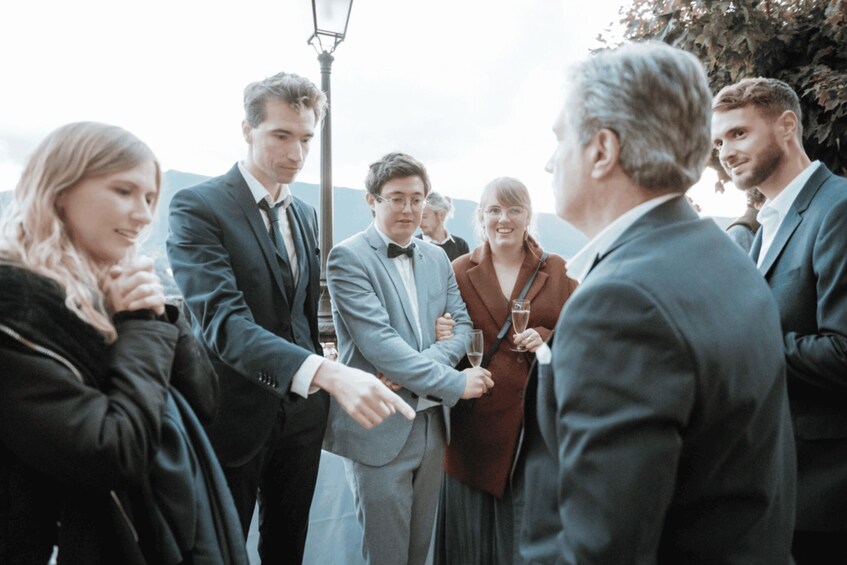 A group of people in formal attire standing outdoors, possibly at a social event. 4