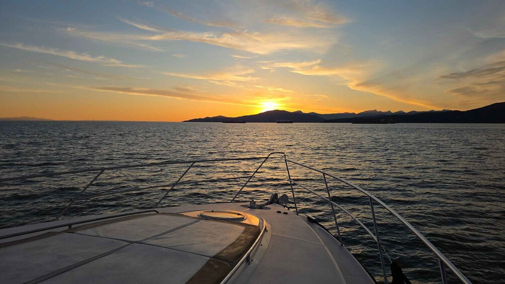 A boat's deck with a view of a sunset over water and distant mountains. 2