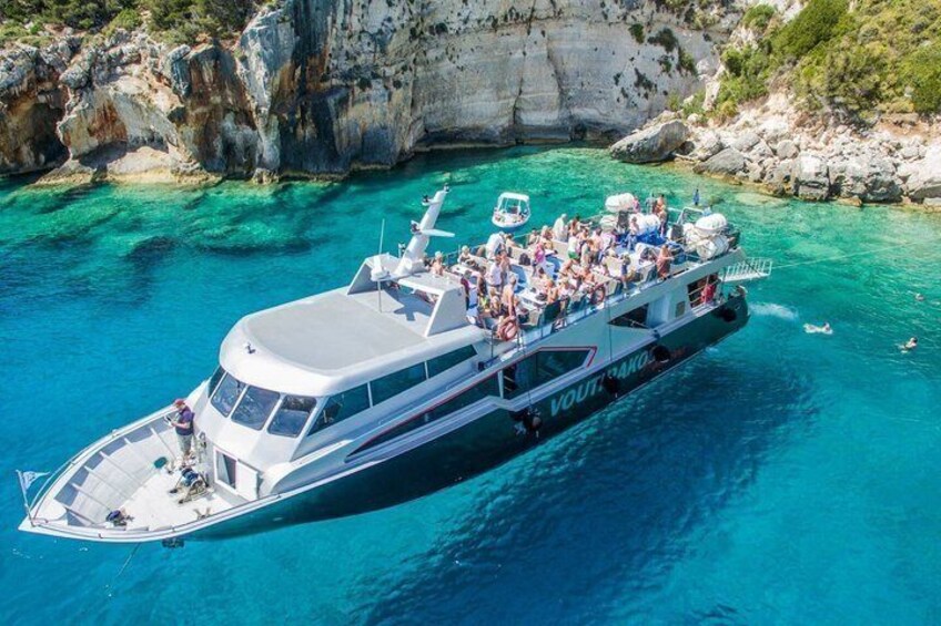 A large boat with passengers, surrounded by clear blue waters and rocky cliffs. 5