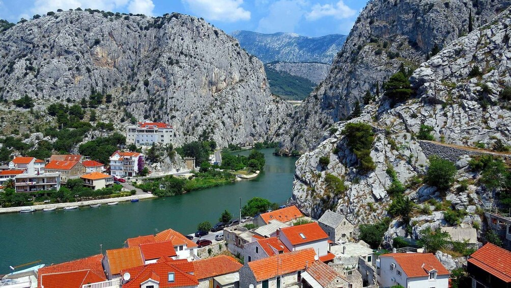 A coastal town with red-roofed buildings, a river, and rocky mountains in the background. 3