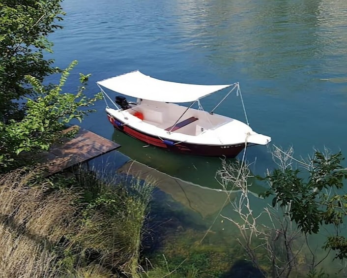 A small boat docked at a pier with a white canopy, surrounded by calm water and greenery. 2