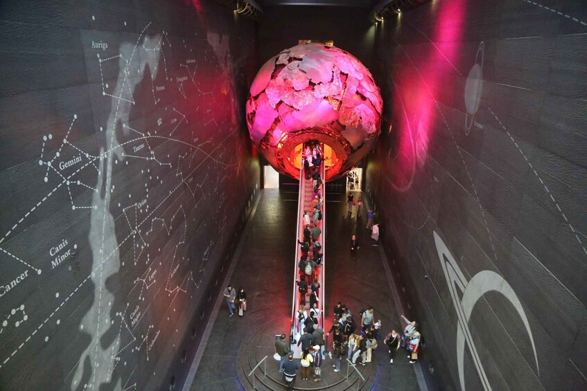 A large spherical structure with a red interior, surrounded by a dark room with a star map on the walls. 4