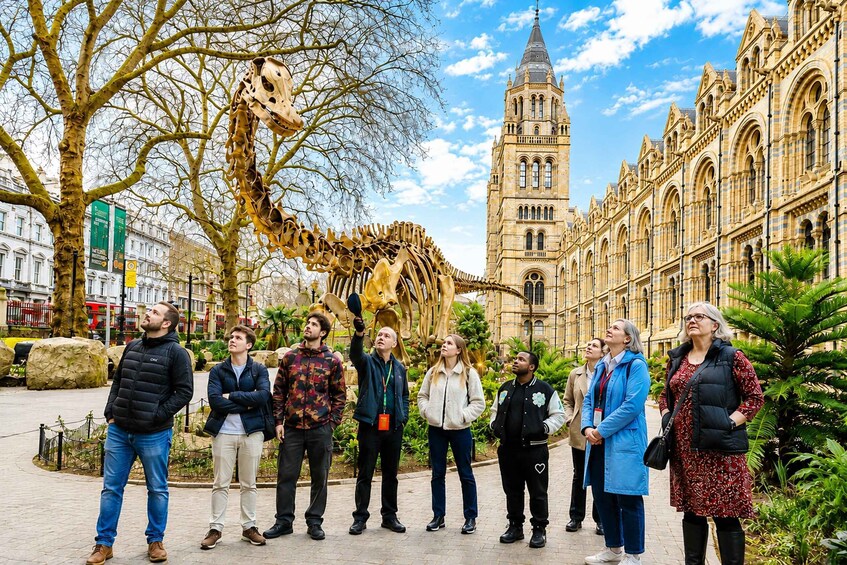 A group of people standing in a plaza with a large giraffe sculpture and historic buildings in the background. 1