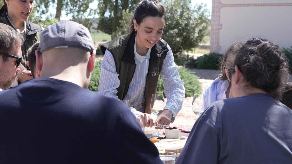 A group of people gathered around a table with food and drinks, outdoors with trees in the background. 1