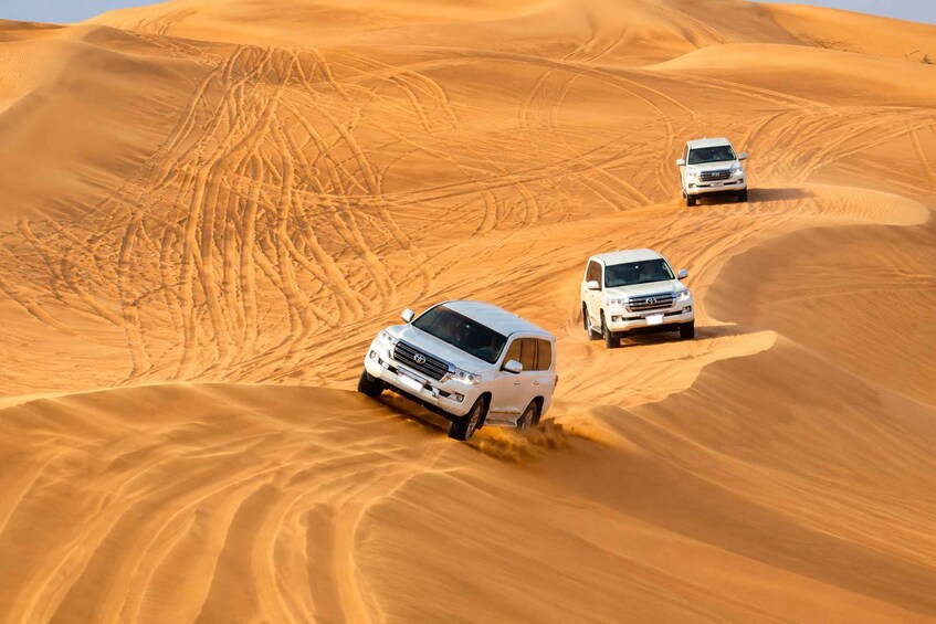 Three white SUVs navigating a sandy desert landscape with undulating dunes. 4