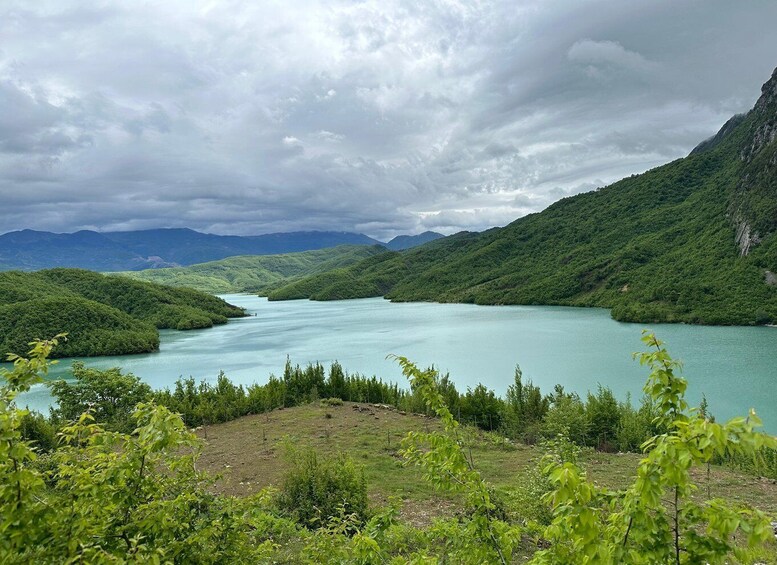 A turquoise lake surrounded by lush green hills and mountains under a cloudy sky. 2