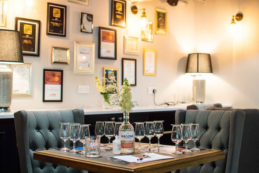 A dining table with wine glasses and a bottle of Masons gin, set in a room with framed awards on the wall. 2