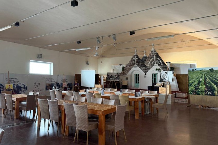A spacious room with tables and chairs, a projector screen, and a mural of a vineyard. 2