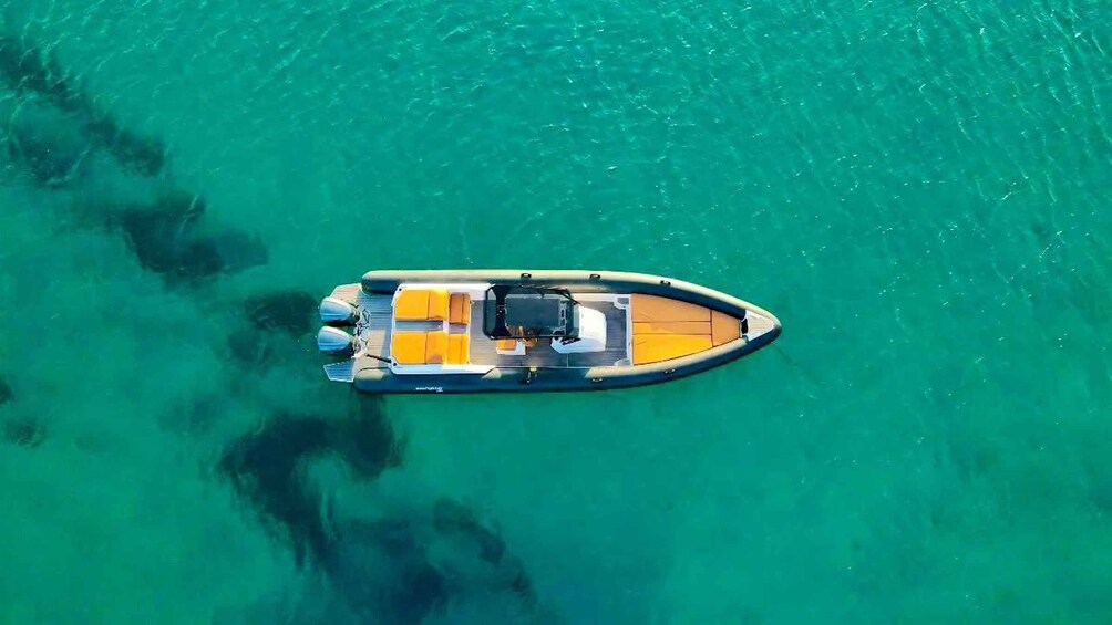 An aerial view of a small motorboat with a wooden deck and two outboard motors on clear turquoise water. 1
