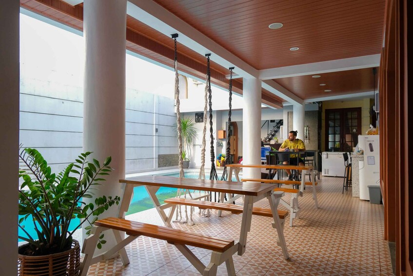 A poolside area with wooden tables and chairs, a hanging chair, and a potted plant. 5