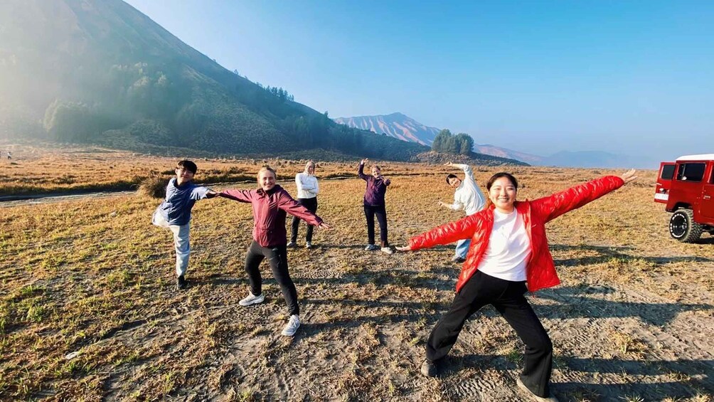 A group of people performing a dance in a field with mountains in the background. 2