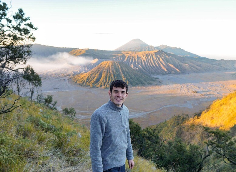 A person standing on a hillside overlooking a volcanic landscape with a mountain in the background. 5
