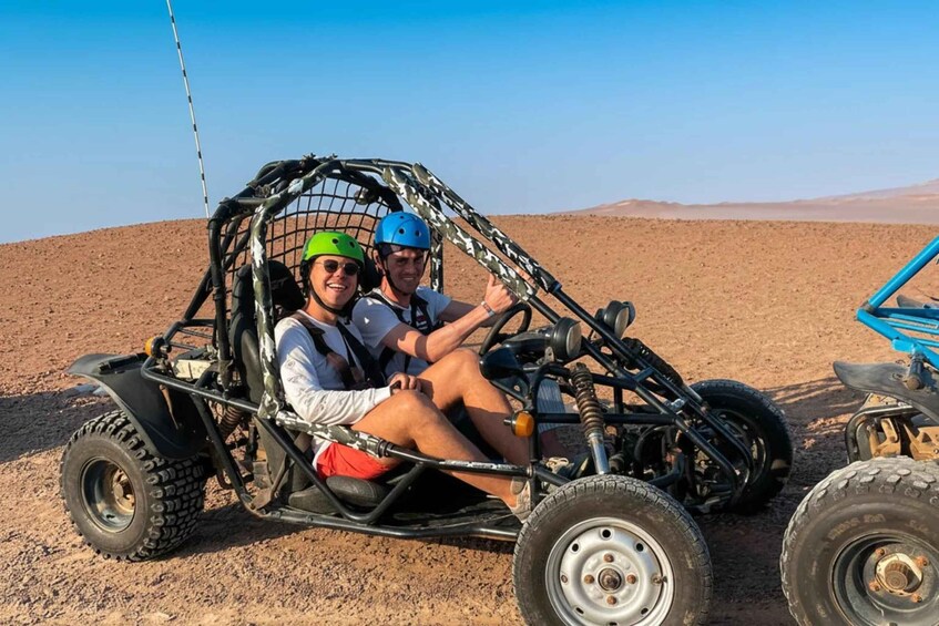 To personer i en ørkenbuggy med et let konstrueret kaleche på en jordvej. 1