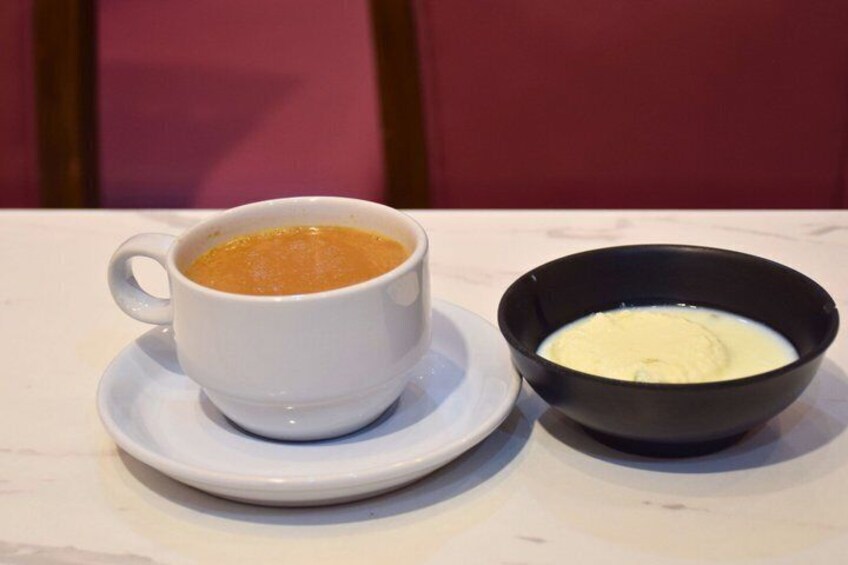 A white cup of coffee and a black bowl of yogurt on a white table. 2