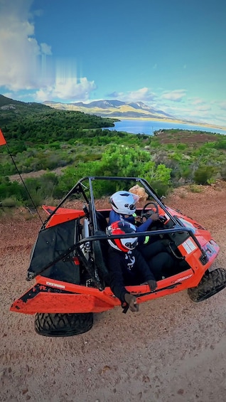 A red off-road vehicle parked on a dirt path with a scenic view of mountains and a lake in the background. 2