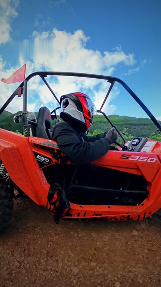 A person in a red ATV with a black and white helmet, driving on a dirt road. 4