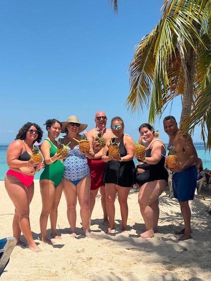 A group of people on a sandy beach holding pineapples. 2